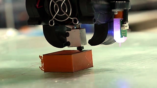 Nozzle extruding orange filament on dual-colour cube (SKU ask)