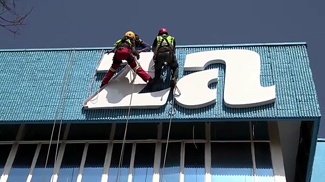 Rope-access techs mounting white am.co.za letters on blue facade (SKU ask)