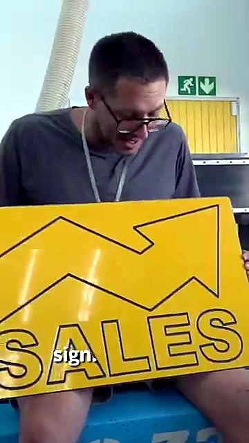Presenter holds finished yellow SALES sign (SKU ask)