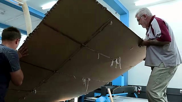Two operators lifting full-size spoilboard sheet (SKU ask)