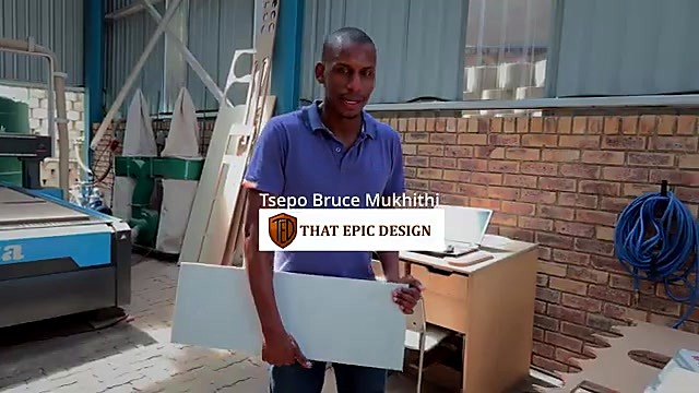 Tsepo Bruce Mukhithi of That Epic Design in the workshop holding a stone panel, CNC router behind