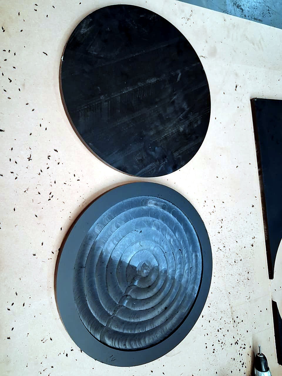 R-2030K/55L EasyRoute: CNC-cut black plastic discs, one with a stepped concentric pocket/rebate, on the spoilboard (cut sample, staff still)