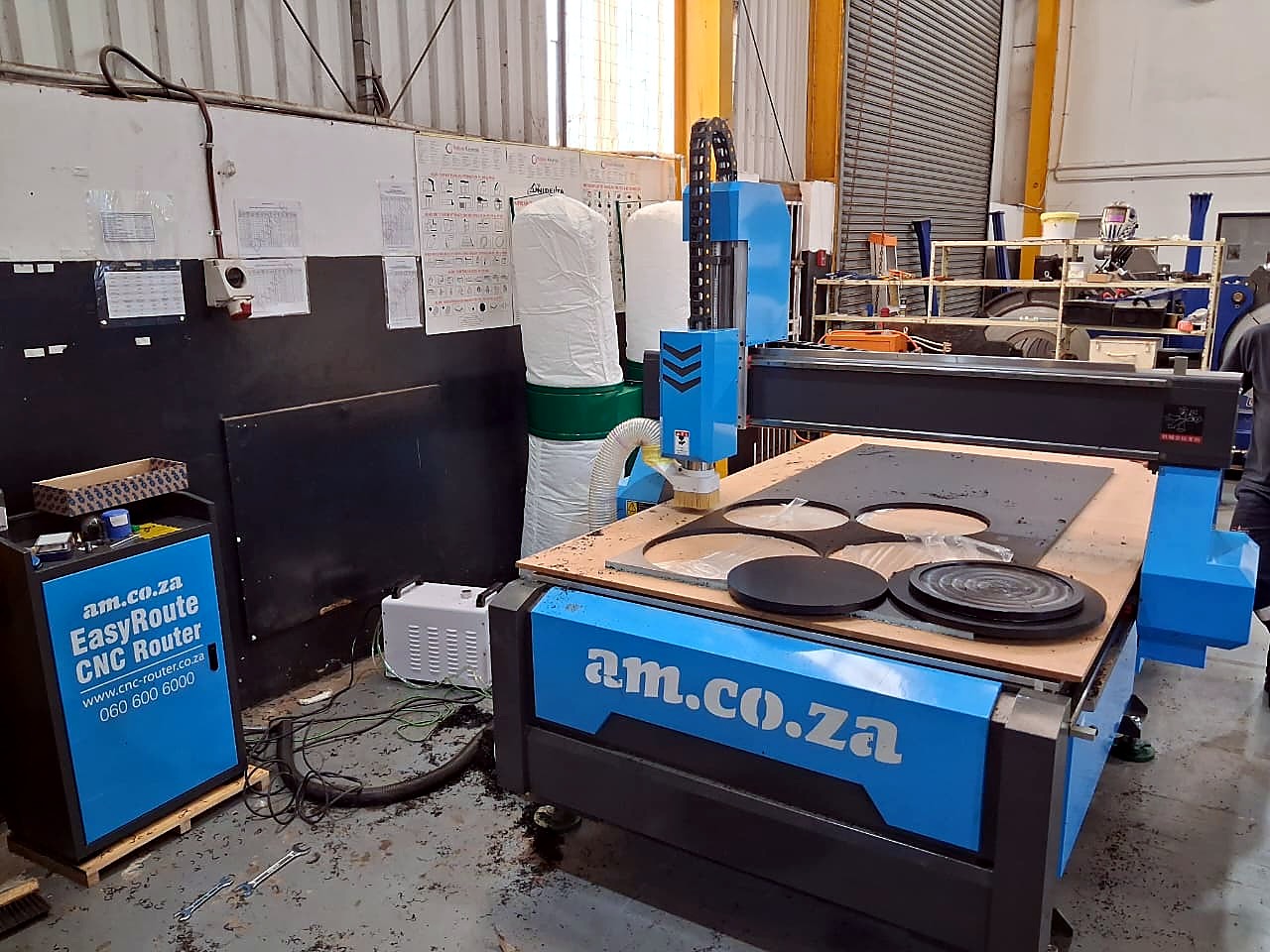 R-2030K/55L EasyRoute: blue am.co.za CNC router in the workshop with black plastic discs cut on the vacuum table (staff still)