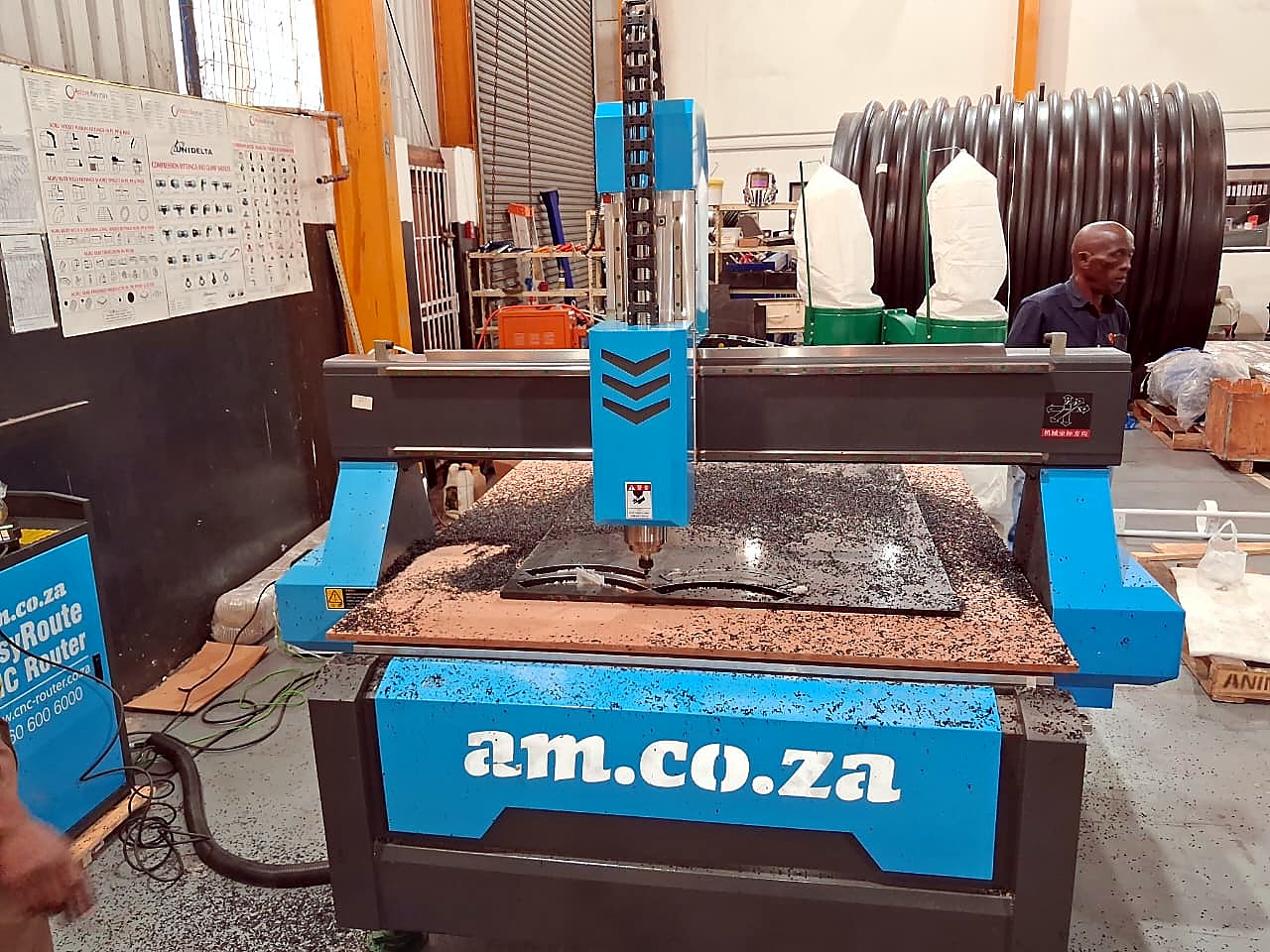 R-2030K/55L EasyRoute: blue am.co.za CNC router with gantry over a machined sheet on the vacuum table, in the workshop (staff still)