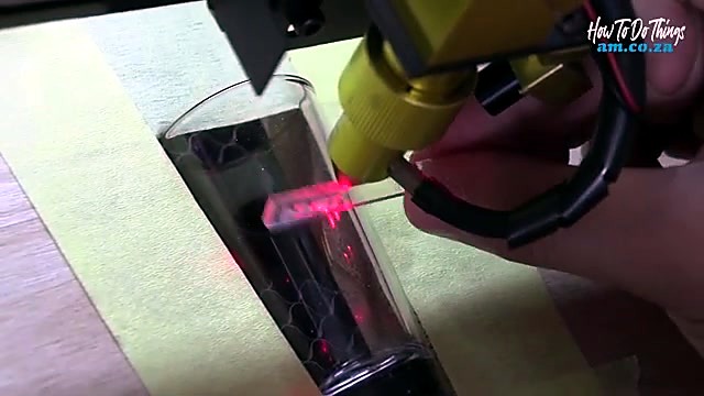 Yellow laser head + red pilot aligned on dark glass (SKU ask)