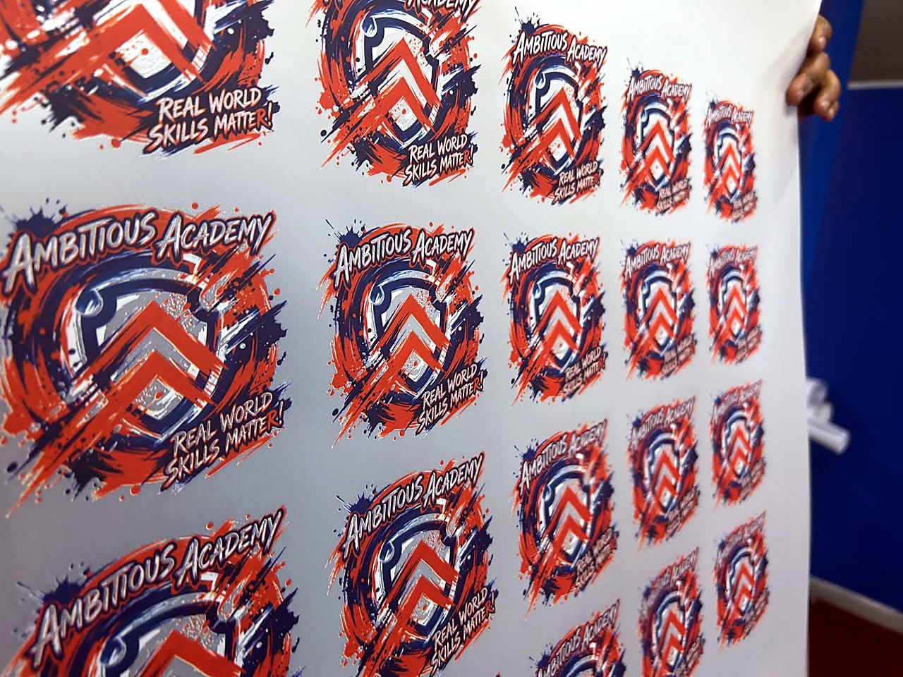 H-DTF/600 DTF: printed and powdered DTF film sheet with rows of 'Ambitious Academy' logos in several sizes, ready for heat-press transfer (staff still)