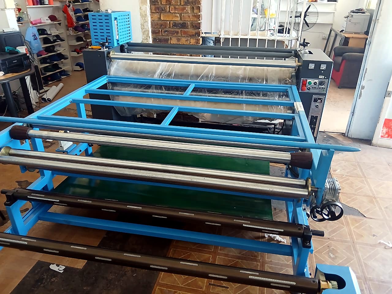 H-ROLLER/1700/OIL9: machine identity — blue frame, control panel, green belt, plastic-wrapped drum (staff still)
