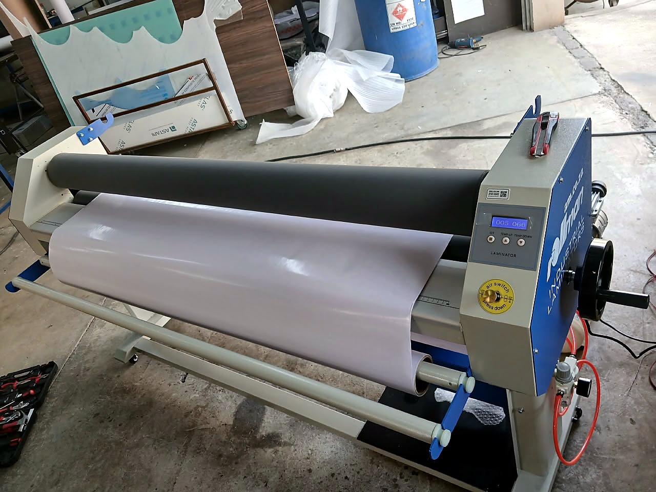RM-1520 Rollman laminator: white laminating film fed between grey rubber rollers, blue side panel with LCD control and red air lines (staff still)