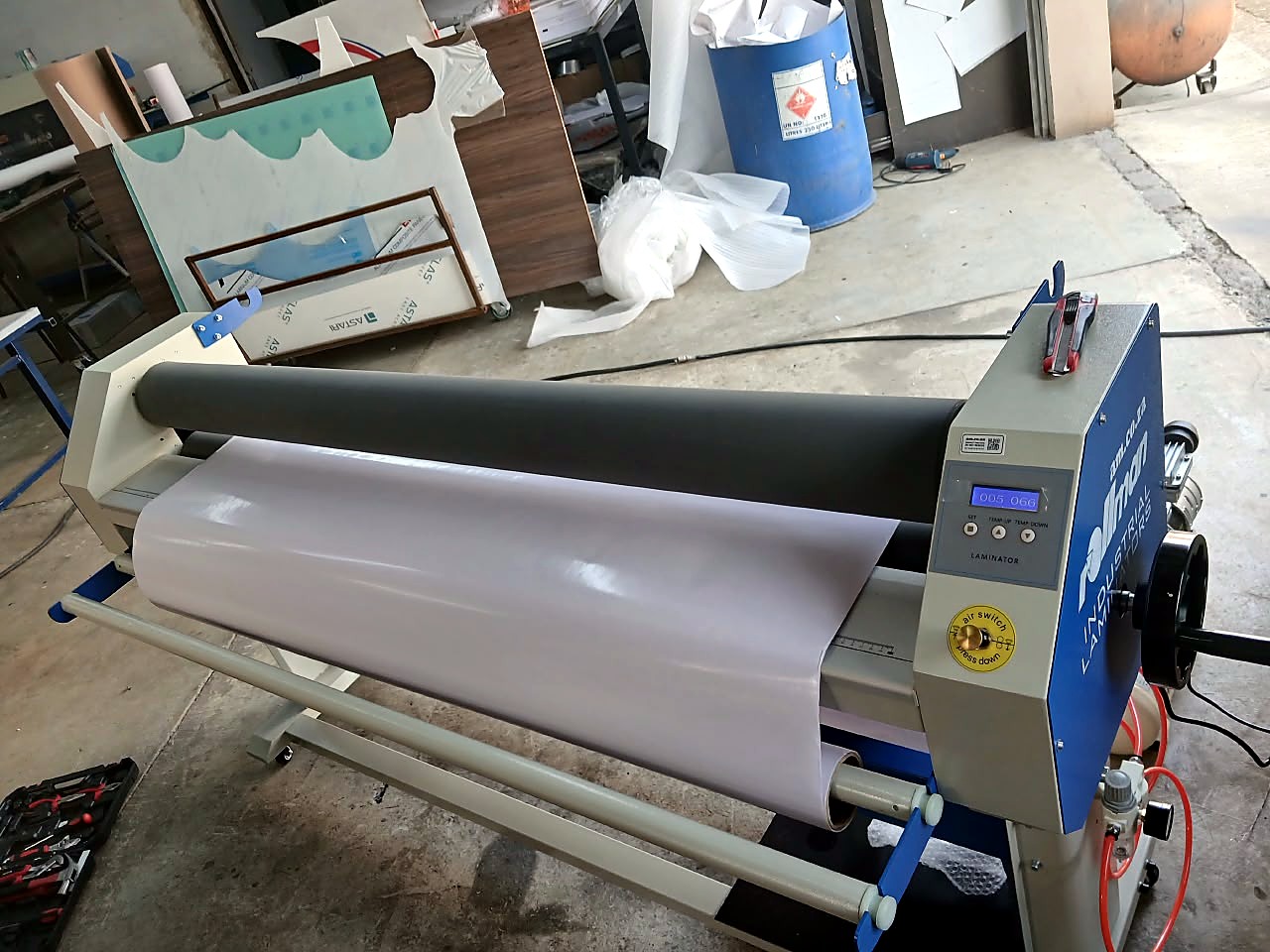 RM-1520 Rollman laminator: front-angle view of film across the rollers with lower supply/feed shafts and blue end brackets (staff still)