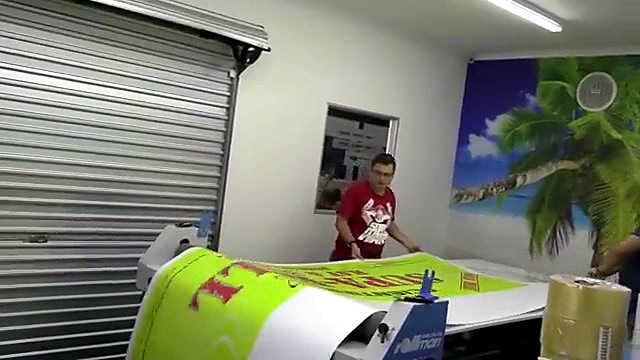 Operators guiding print through wide laminator (SKU ask)