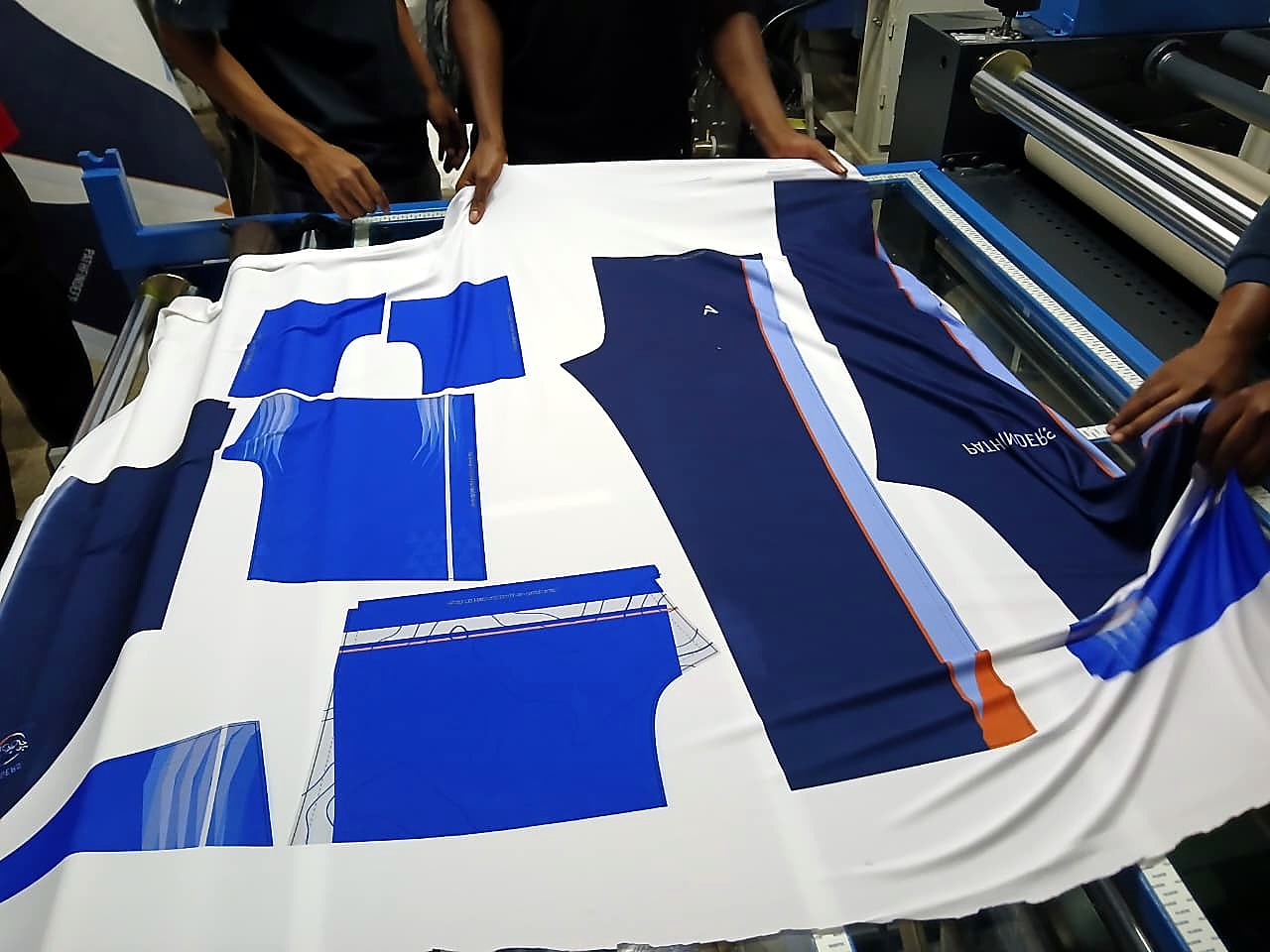 F1-1801/SUB sample output: dye-sublimated sportswear garment panels in blue/navy on white polyester fabric, coming off the rotary heat press (staff still)