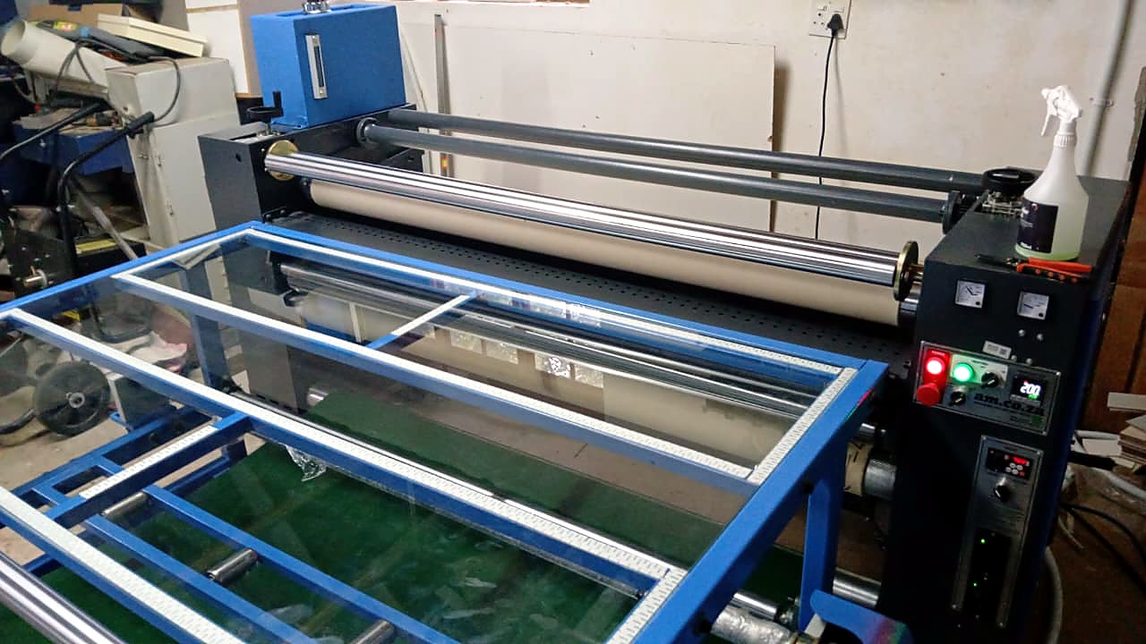 F1-1801/SUB sublimation workflow: rotary calender heat press (am.co.za control panel at 200 degrees) with glass feed table, used to transfer prints from the 1800mm sublimation printer (staff still)