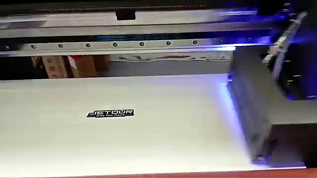 UV-DTF printhead carriage with violet UV glow printing a black logo on film