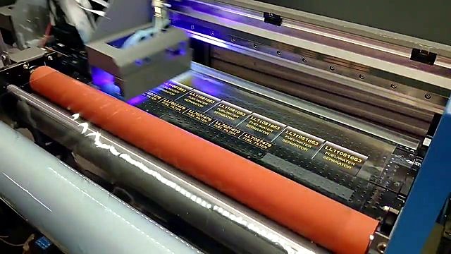 Label rows feeding under orange laminate roller (SKU ask)